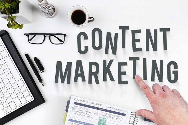 Schriftzug Content Marketing auf einem Schreibtisch mit Brille, Laptop und Kuli
